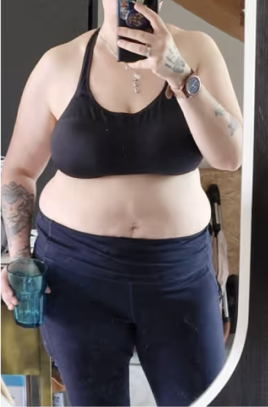Eine Frau in Sport-BH und Shorts hält eine Tasse in der Hand.