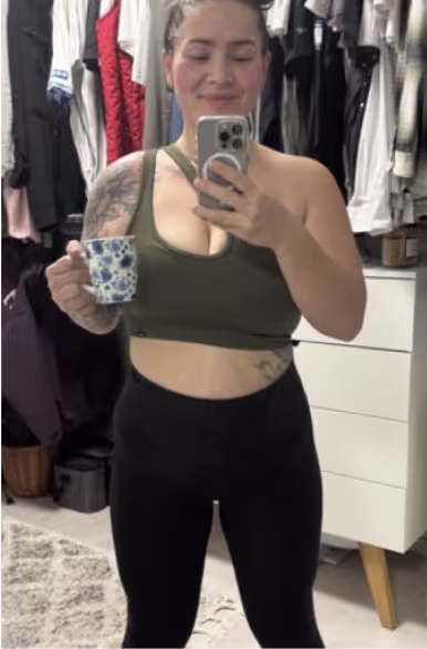 Eine Frau in Sport-BH und Shorts hält eine Tasse in der Hand.