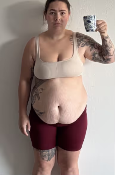 Eine Frau in Sport-BH und Shorts hält eine Tasse in der Hand.