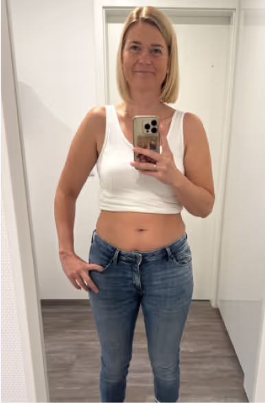 Eine blonde Frau in Jeans und weißem Oberteil macht ein Selfie im Spiegel.