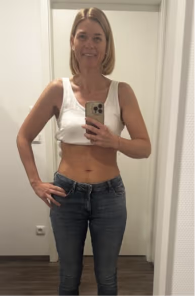 Eine blonde Frau in Jeans und weißem Oberteil macht ein Selfie im Spiegel.