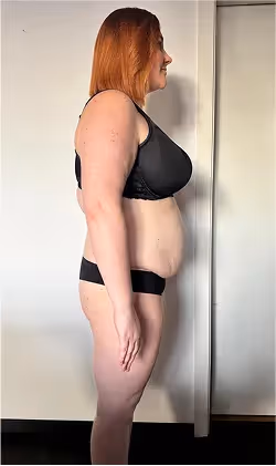 Eine Frau mit roten Haaren in Sport-BH und Unterwäsche steht seitlich.