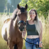 WPF Community - Eine lächelnde Frau mit langen Haaren steht neben einem Pferd in einem Feld.
