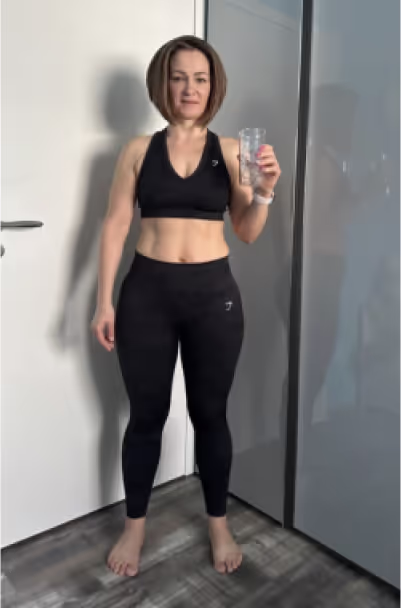 Eine Frau in schwarzer Sportkleidung steht vor einer weißen Tür und hält ein Glas.