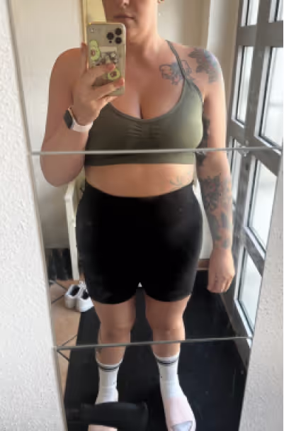 Eine Frau in Sport-BH und Shorts macht ein Selfie im Spiegel.