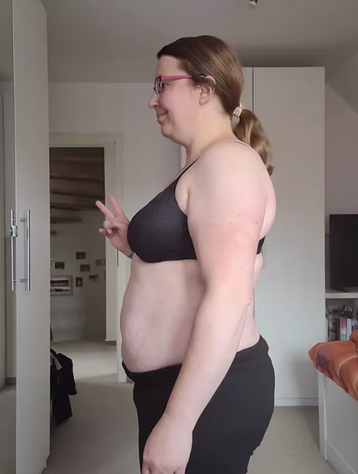 Eine lächelnde Frau in Sport-BH und Hose zeigt das Friedenszeichen.